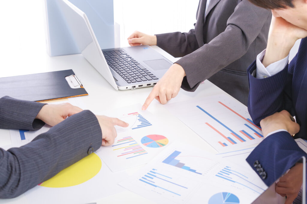 市場調査のデータ（グラフや円グラフ）を囲んで議論する商品企画担当者